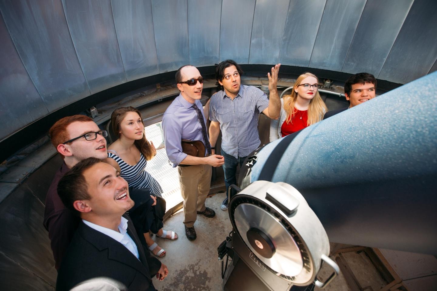 Group of students gazing up large telescope in lab