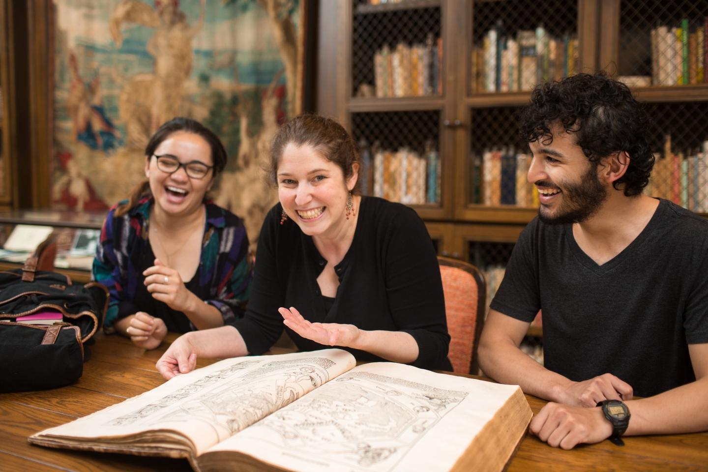 Students laugh as they examine a large, ancient book in Trinity's Special Collections.