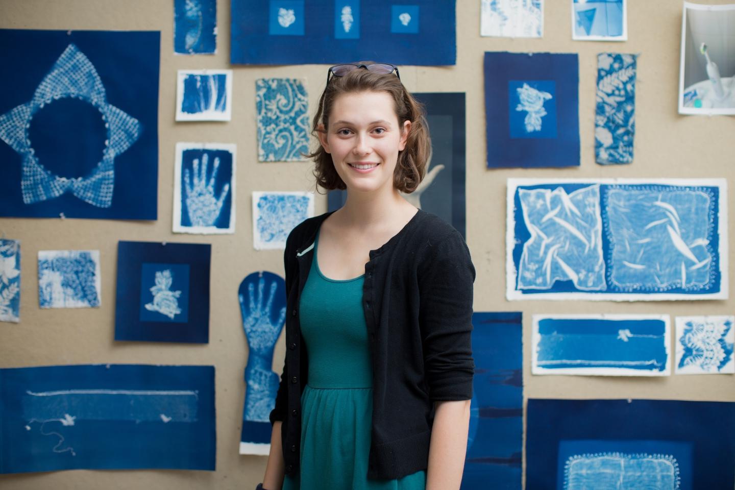 photo of artist Sasha Faust standing in front of some of her works