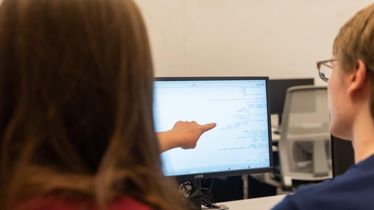 one student pointing at computer screen as other student looks on